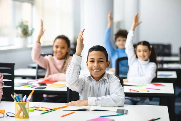 Diverse kleine scholieren steken de hand op in de klas — Stockfoto