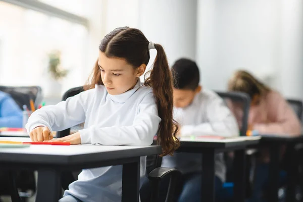 Portrait of small girl sitting at desk in classroom — Stock Photo, Image