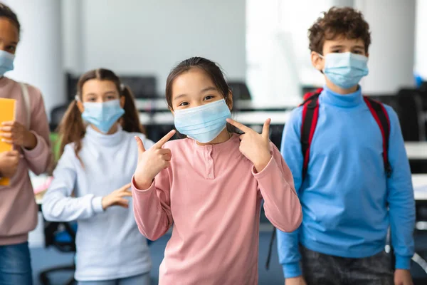 Asian girl in medical mask pointing at her face