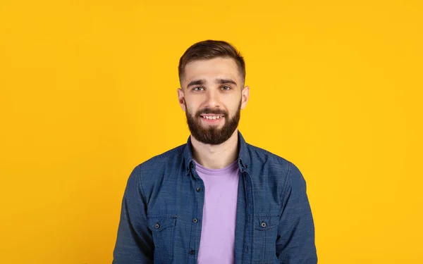 Chico joven despreocupado mirando a la cámara y sonriendo sobre fondo de estudio naranja, panorama —  Fotos de Stock