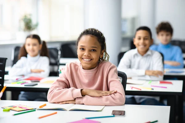 Retrato de pequena menina negra sentada na mesa em sala de aula — Fotografia de Stock