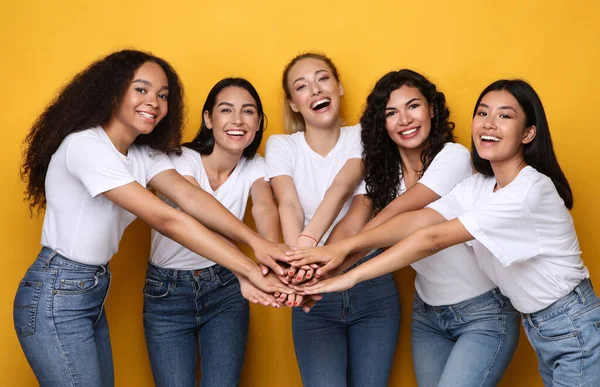 Cinco mulheres multiétnicas felizes segurando as mãos posando em fundo amarelo — Fotografia de Stock