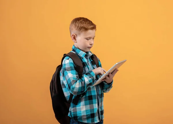 Ginger kid schooler met behulp van digitale tablet op geel — Stockfoto