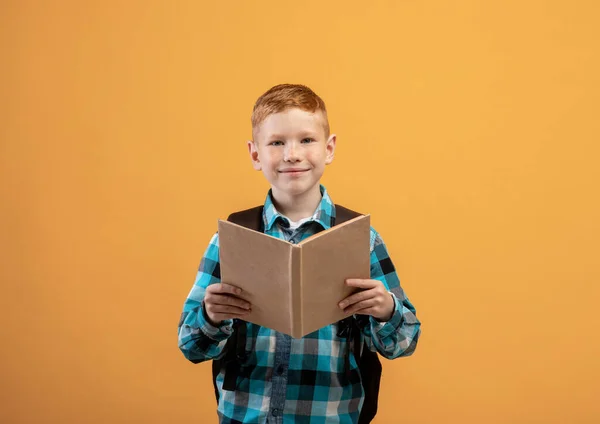 Söt ingefära barn skolkare läsa bok, gul studio bakgrund — Stockfoto