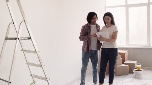 Jonge vrouw en echtgenoot kiezen decoratie ideeën voor nieuw appartement, bespreken herontwerpen huis met ontwerp plan — Stockvideo