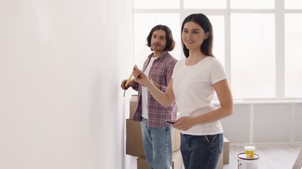 Ženatý muž a žena měřicí stěny s lepicí páskou dohromady, dělá domácí zlepšení a renovace — Stock video