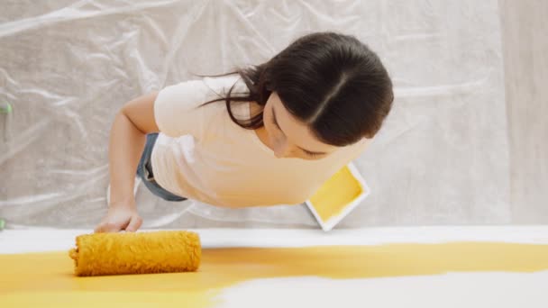 Mujer joven sala de renovación, pintura de pared blanca con rodillo amarillo, sonriendo a la cámara, plano de vista superior — Vídeos de Stock