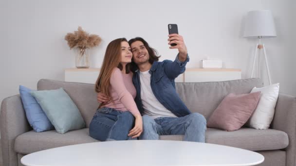 Młoda, milenijna para zakochana w sobie, robiąca selfie razem, pozująca i gryząca do kamery komórkowej w domu, spowolniona — Wideo stockowe