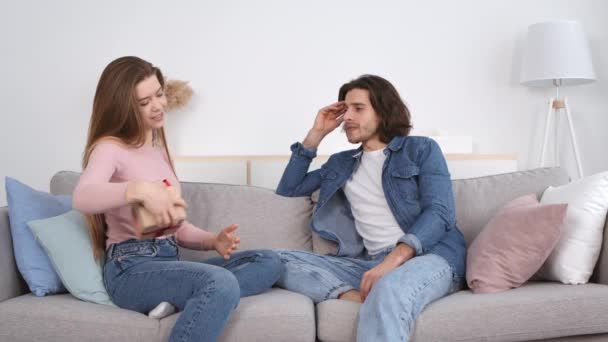 Młoda kobieta gratuluje mężowi prezentu i przytula go, siedzi na kanapie w domu, w zwolnionym tempie — Wideo stockowe