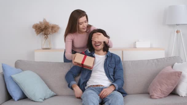 Mujer joven cerrando los ojos de su novio y dándole un regalo sorprendente, felicitación con vacaciones — Vídeo de stock