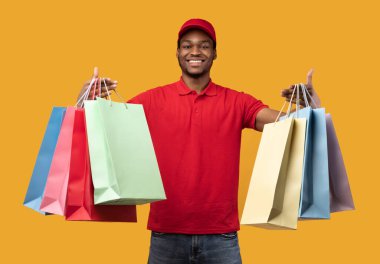 Stüdyoda renkli çantalar taşıyan siyah teslimatçı.