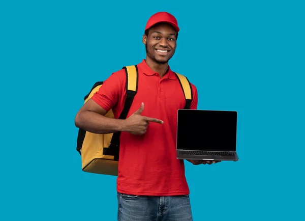 Uomo di consegna nero che tiene il computer portatile con schermo vuoto per il mockup — Foto Stock