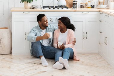 Romantik siyah çift mutfakta yerde kahve içiyor, birlikte vakit geçiriyorlar.