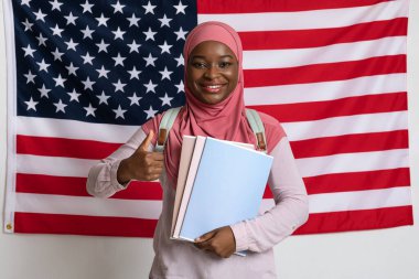 tesettürlü gülümseyen kadın başparmağını Amerikan bayrağında gösteriyor.