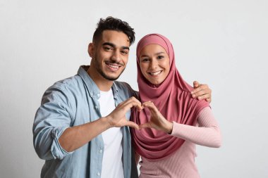 Elleriyle kalp hareketi yapan romantik Müslüman çiftin portresi.