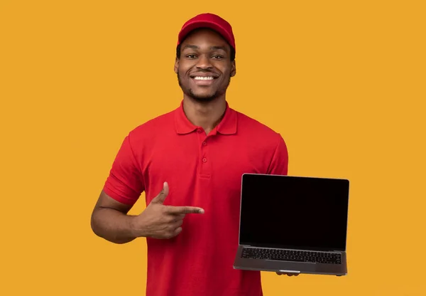 Black delivery man holding laptop with blank screen for mockup — Stock Photo, Image