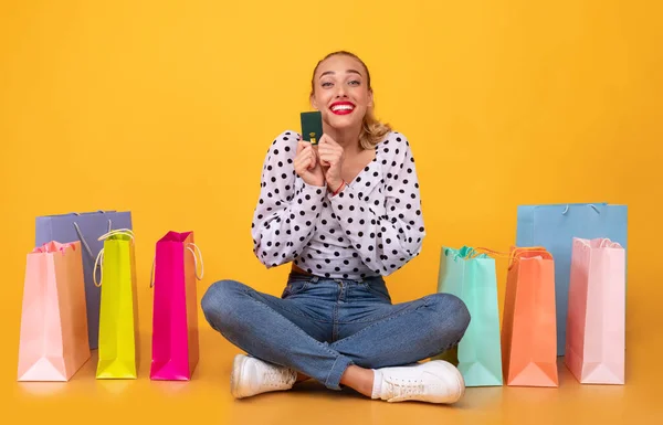 Donna felice che tiene la carta di credito seduta con borse della spesa — Foto Stock