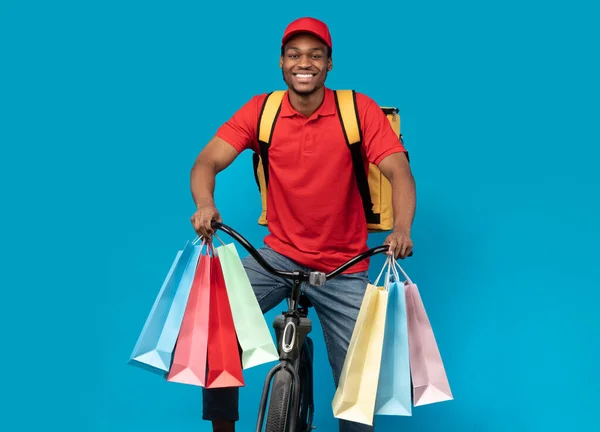 Lächelnder schwarzer Zusteller auf Fahrrad mit Einkaufstaschen — Stockfoto