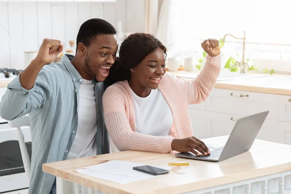 Vencedores da sorte. Entusiasmado casal afro-americano com laptop na cozinha celebrando o sucesso — Fotografia de Stock
