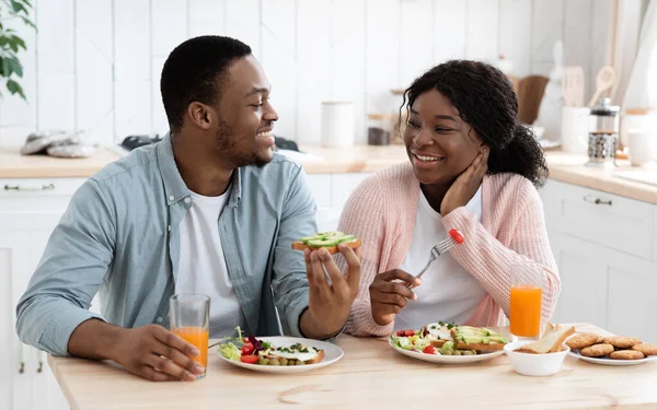 Cónyuges negros positivos comiendo sabroso desayuno y beber jugo de naranja en la cocina — Foto de Stock