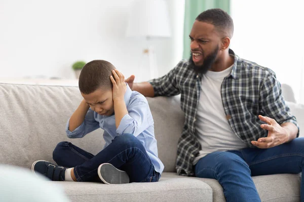 Злой африканский отец кричит на испуганного сына, сидящего дома — стоковое фото