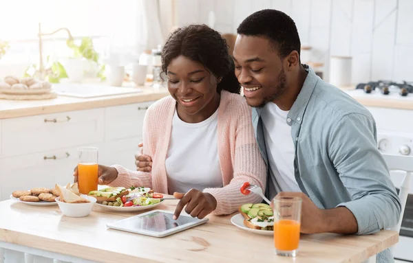 Ευτυχισμένο μαύρο ζευγάρι χρησιμοποιώντας ψηφιακή ταμπλέτα, ενώ έχοντας πρωινό στην κουζίνα — Φωτογραφία Αρχείου