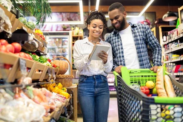 Família negra comprando alimentos tomando notas na lista de verificação no supermercado — Fotografia de Stock