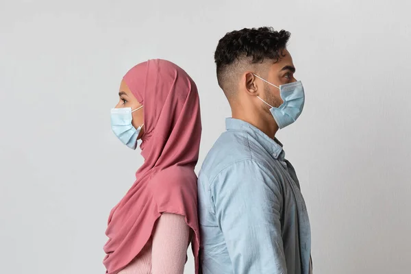 Coronavirus概念。年轻的穆斯林夫妇背着医疗面具背靠背地站着 — 图库照片