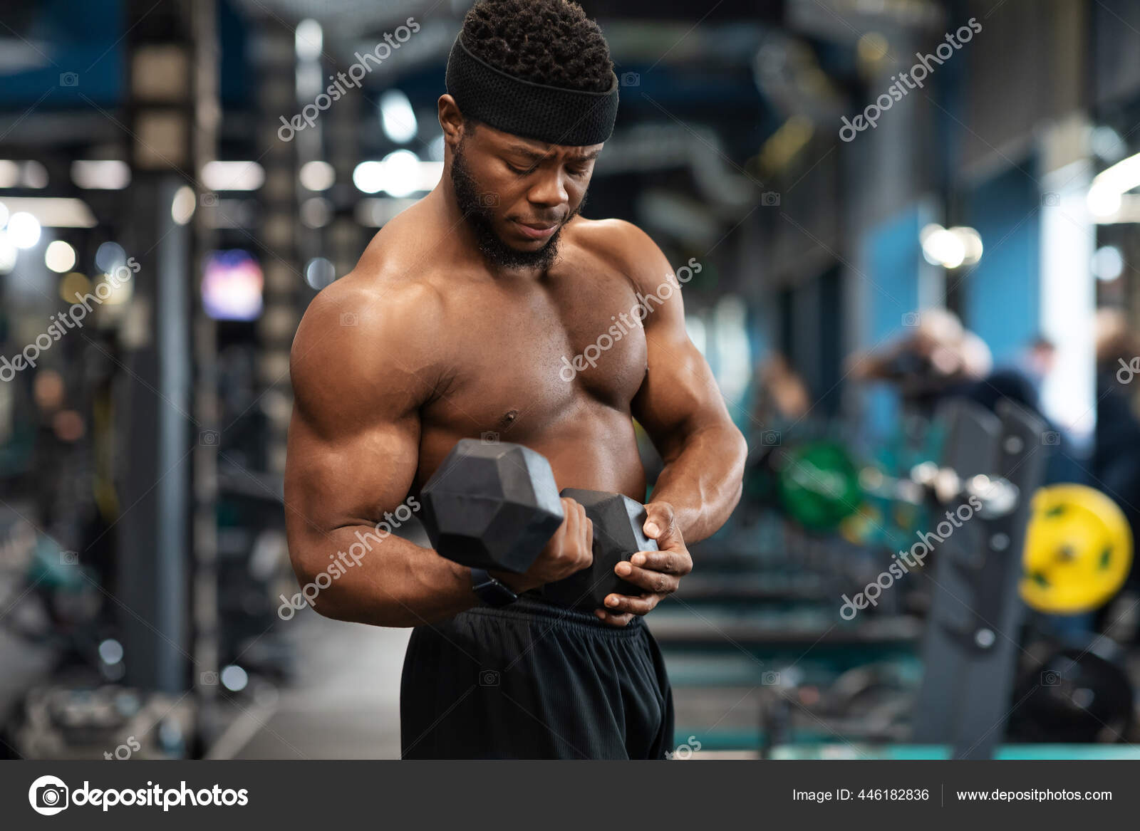 Concentrated black athlete training arms with dumbbells at gym