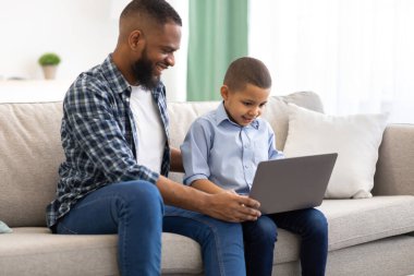 Afrikalı baba ve oğul evde otururken dizüstü bilgisayar kullanıyor.