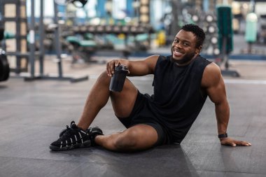 Yerde oturan mutlu siyah vücut geliştirici.