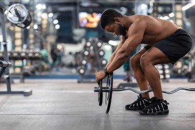 Spor salonunda ağırlık kaldıran siyah kaslı adamın yan görüntüsü