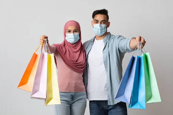 Pandemické nakupování, veselý muslim pár v ochranných lékařských maskách ukazuje nákupní tašky — Stock fotografie