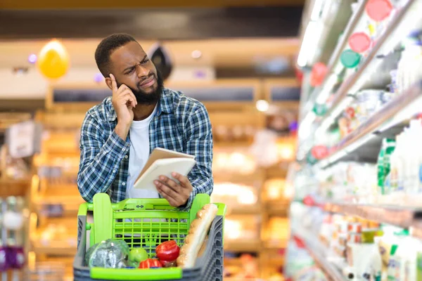 African Man Buying Food With Groceries Checklist Standing In Supermarket