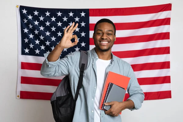 Lächelnder schwarzer Student steht über amerikanischer Flagge und zeigt Okay — Stockfoto