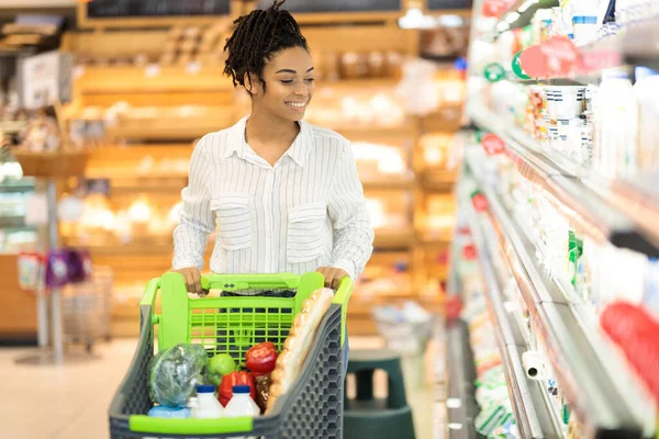 棚に沿って歩いてスーパーマーケットで食料品の買い物にアフリカの女性 — ストック写真