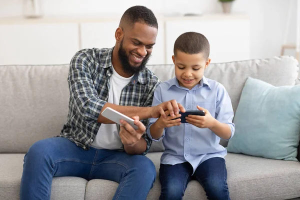 Schwarzer Vater und Sohn mit Smartphones auf Couch im Haus — Stockfoto