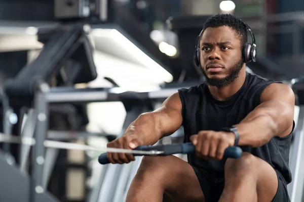 Schöner Sportler trainiert Körper auf modernem Rudergerät im Fitnessstudio — Stockfoto