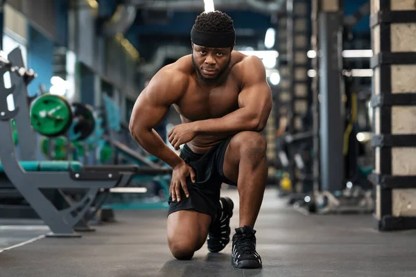 Concentrated black athlete training arms with dumbbells at gym