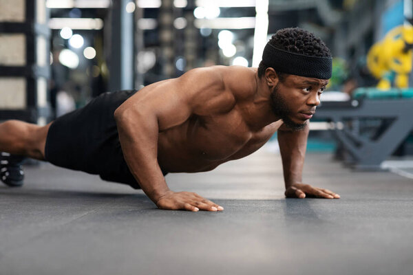 Shirtless black man making push-ups on floor in gym