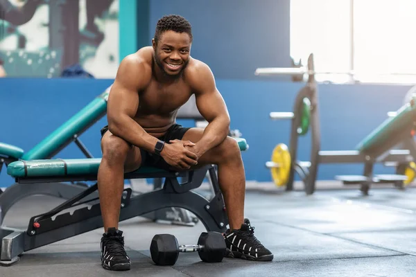 Fröhlicher Schwarzer, der sich nach Bizeps-Training ausruht, Fitnessstudio-Innenraum — Stockfoto