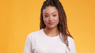 Afro-Amerikan bir kadının kamera karşısında göz kırpan ve gülümseyen, turuncu stüdyo arka planı.