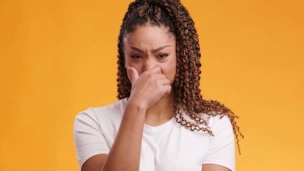 Close up portrait of young african american woman covering her nose from disgusting odor, orange studio background — Stock Video