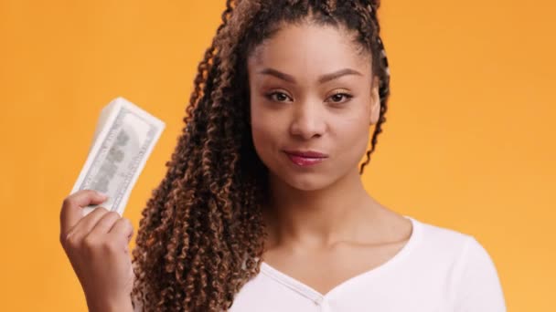 Mega beneficio. Joven mujer afroamericana confiada jugando con la pila de billetes de dólar, fondo de estudio naranja — Vídeos de Stock