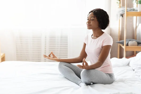 Relaxed black woman sitting on bed and meditating — Stock Photo, Image