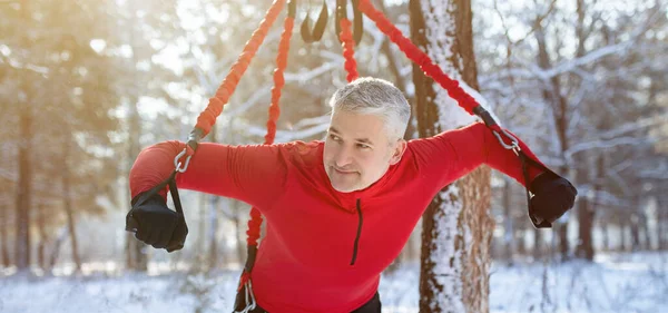 Сильный пожилой человек делает банджи фитнес упражнения, тренировки на открытом воздухе в зимнее утро, панорама — стоковое фото
