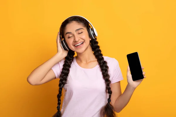 Souriant jeune femme à l'écoute de la musique tenant Smartphone — Photo