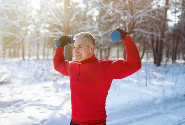 Ανώτερος άνθρωπος γυμνάζεται με αλτήρες έξω το χειμώνα. Ώριμος bodybuilder εργάζονται έξω δικέφαλους του στο χιονισμένο πάρκο — Φωτογραφία Αρχείου