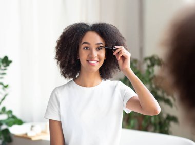 Kadınlar makyaj yapar, kirpiklerini aynanın önünde boyar.