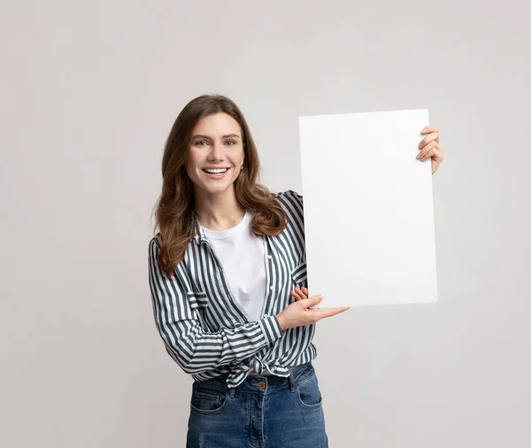 Щаслива молода жінка з чистим плакатом у руках, що передають сіре тло — стокове фото